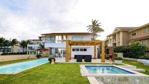 Uma casa moderna com duas piscinas, um terraço coberto e um gramado bem cuidado.