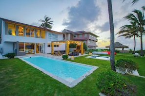 A modern two-story house with a swimming pool, outdoor seating, and a well-maintained lawn.