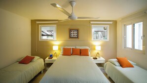Quarto de hotel com uma cama grande, duas mesas de cabeceira, duas luminárias, um ventilador de teto e janelas.