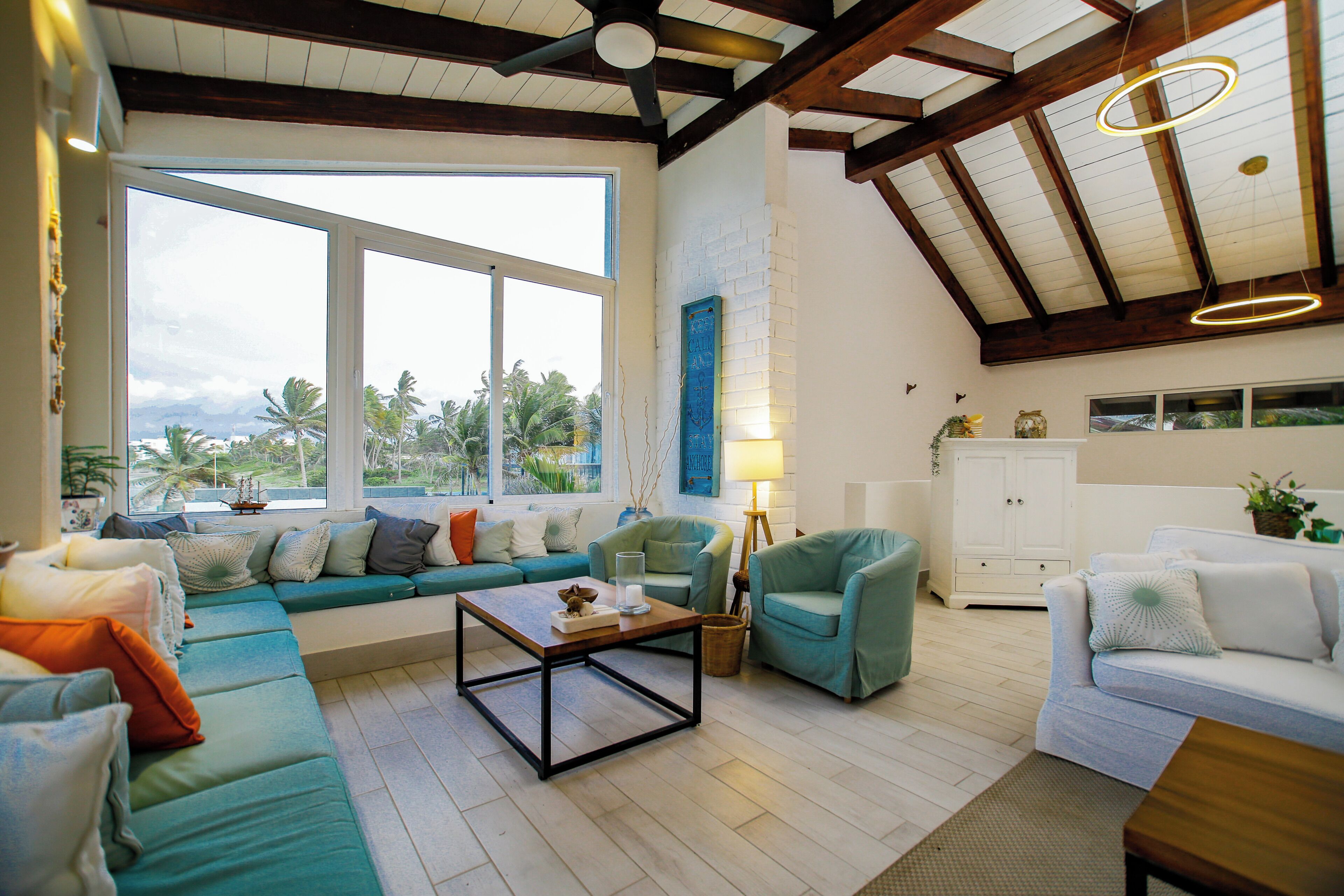 A spacious living room with a large window, a ceiling fan, and a view of palm trees.