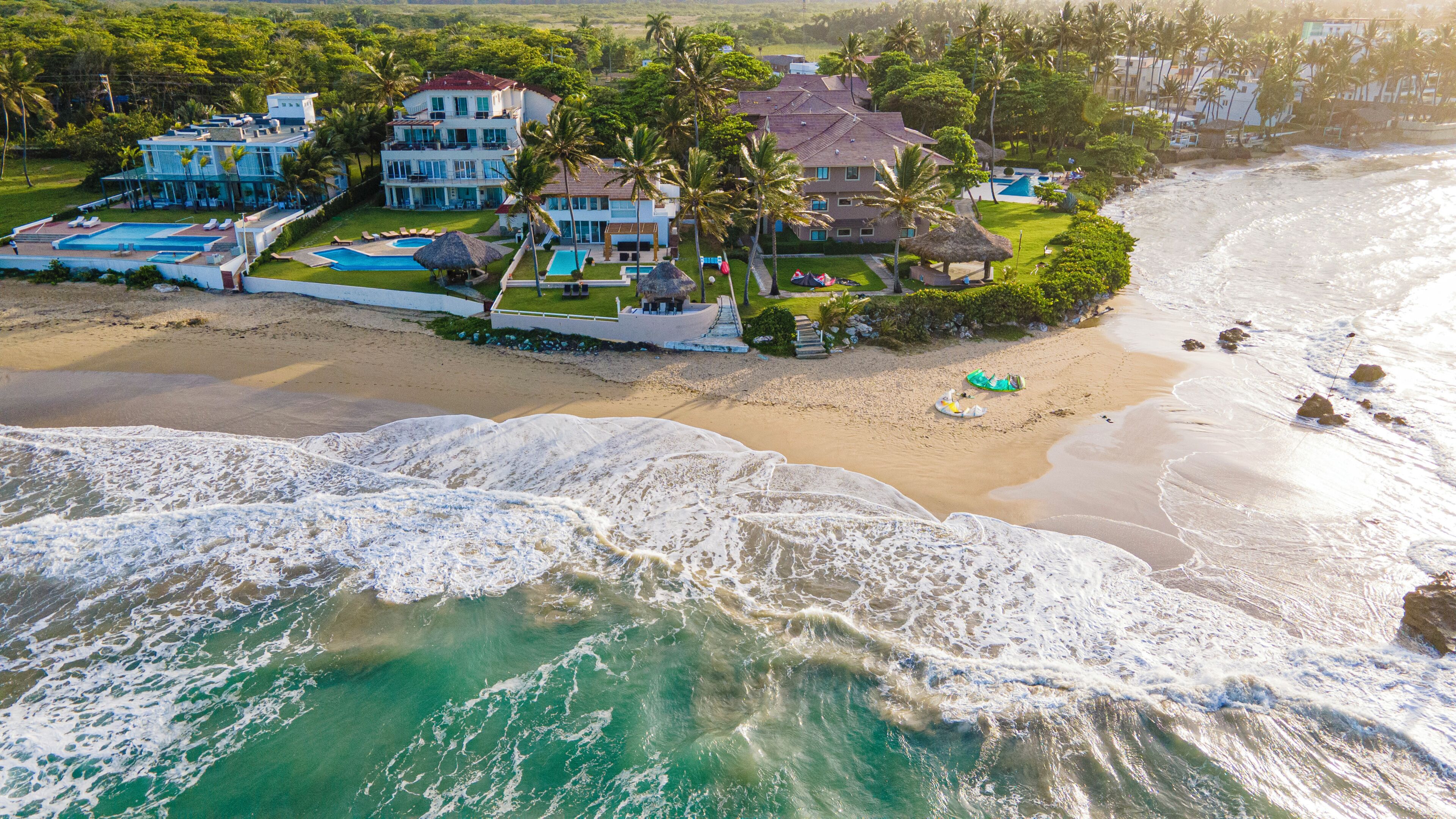 Vista aérea de uma propriedade à beira-mar com várias piscinas, uma praia e uma ampla vista para o oceano.