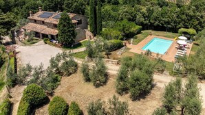Une villa en pierre dotée d’une piscine, entourée d’une végétation luxuriante et de collines.