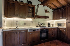 Eine Küche mit Holzschränken, einer Edelstahl-Spüle, einem Herd, einem Backofen und einer Mikrowelle.