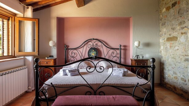 Une chambre à coucher avec un lit, une table de chevet, une lampe fixée au mur, une fenêtre et un mur en pierre.