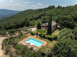 Eine Villa mit Schwimmbad, umgeben von üppiger Vegetation und Hügeln.