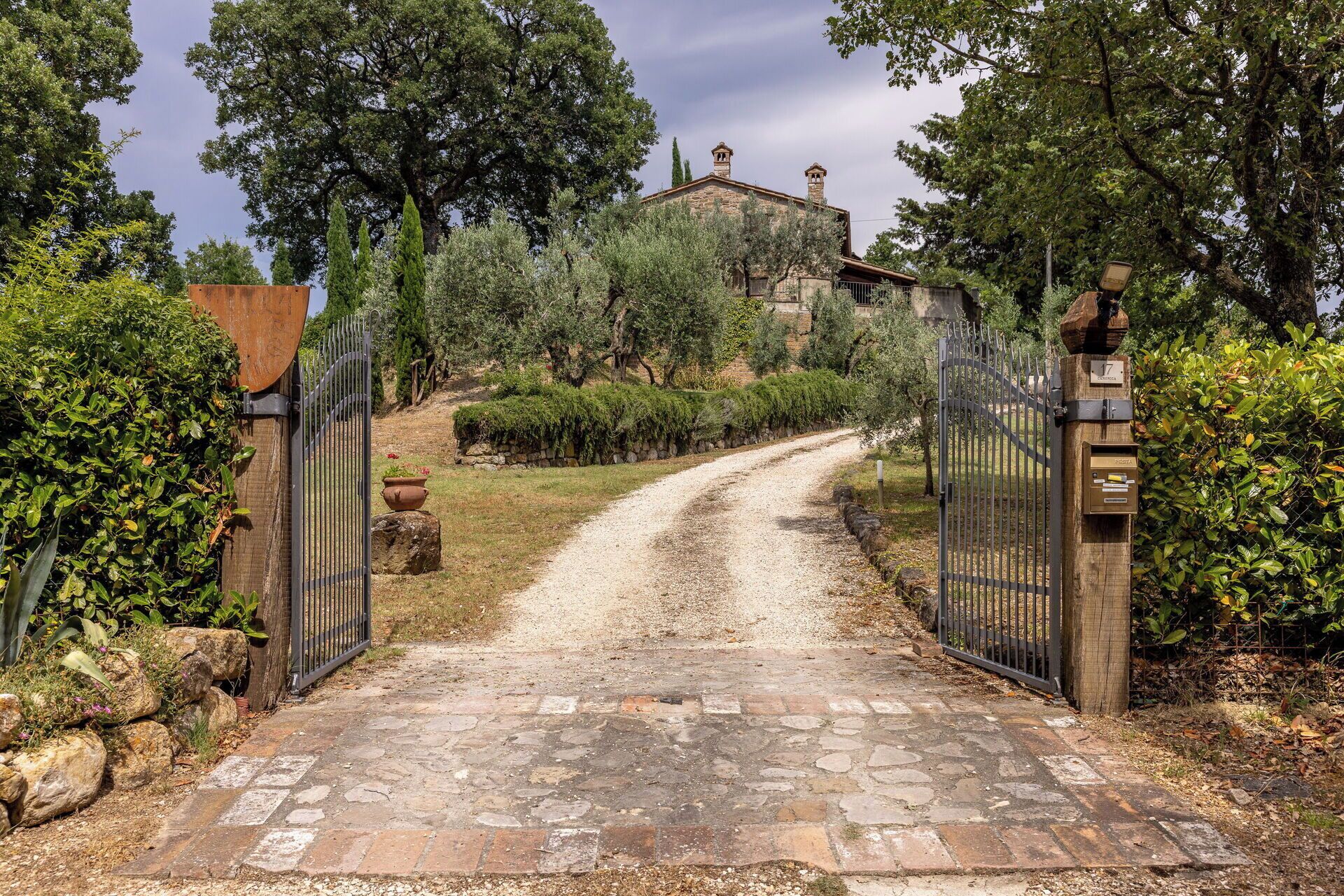 A gravel driveway leading to a gated entrance with a stone building in the background.