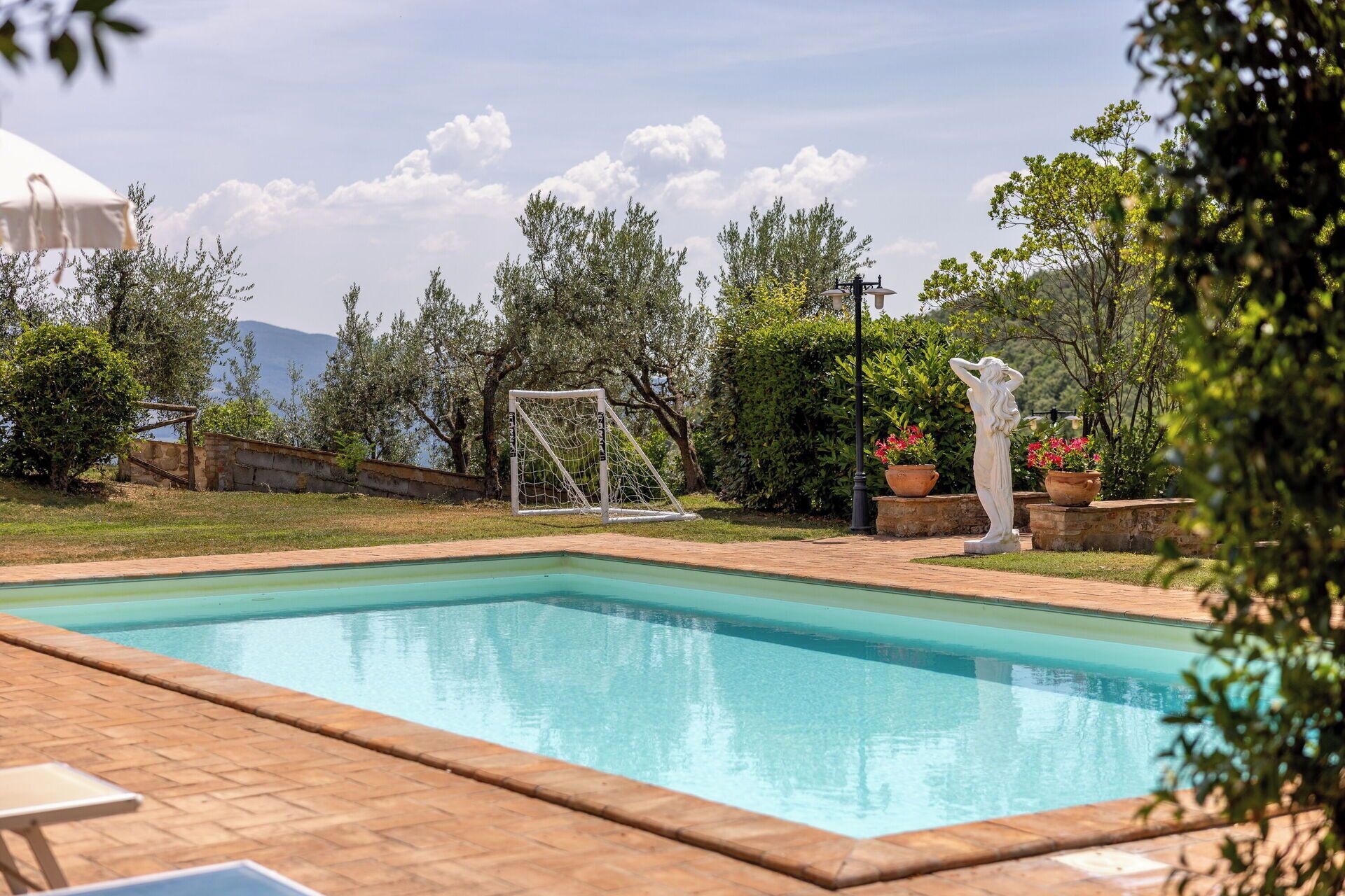 A swimming pool with a netted area, surrounded by greenery and a statue.