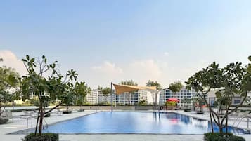 Piscina con borde de baldosas, rodeada de árboles y un edificio con un paraguas rojo.