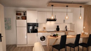 A compact kitchen with a washing machine, a dining area with a table and chairs, and a sofa. - Appartement avec terrasse privée , parking privé, à 7 min des Thermes de Saujon (Saint-Romain-de-Benet)