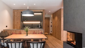 Ein modernes Interieur mit einem Holzes Esstisch, schwarzen Stühlen, einer Hängelampe und einem Kamin.