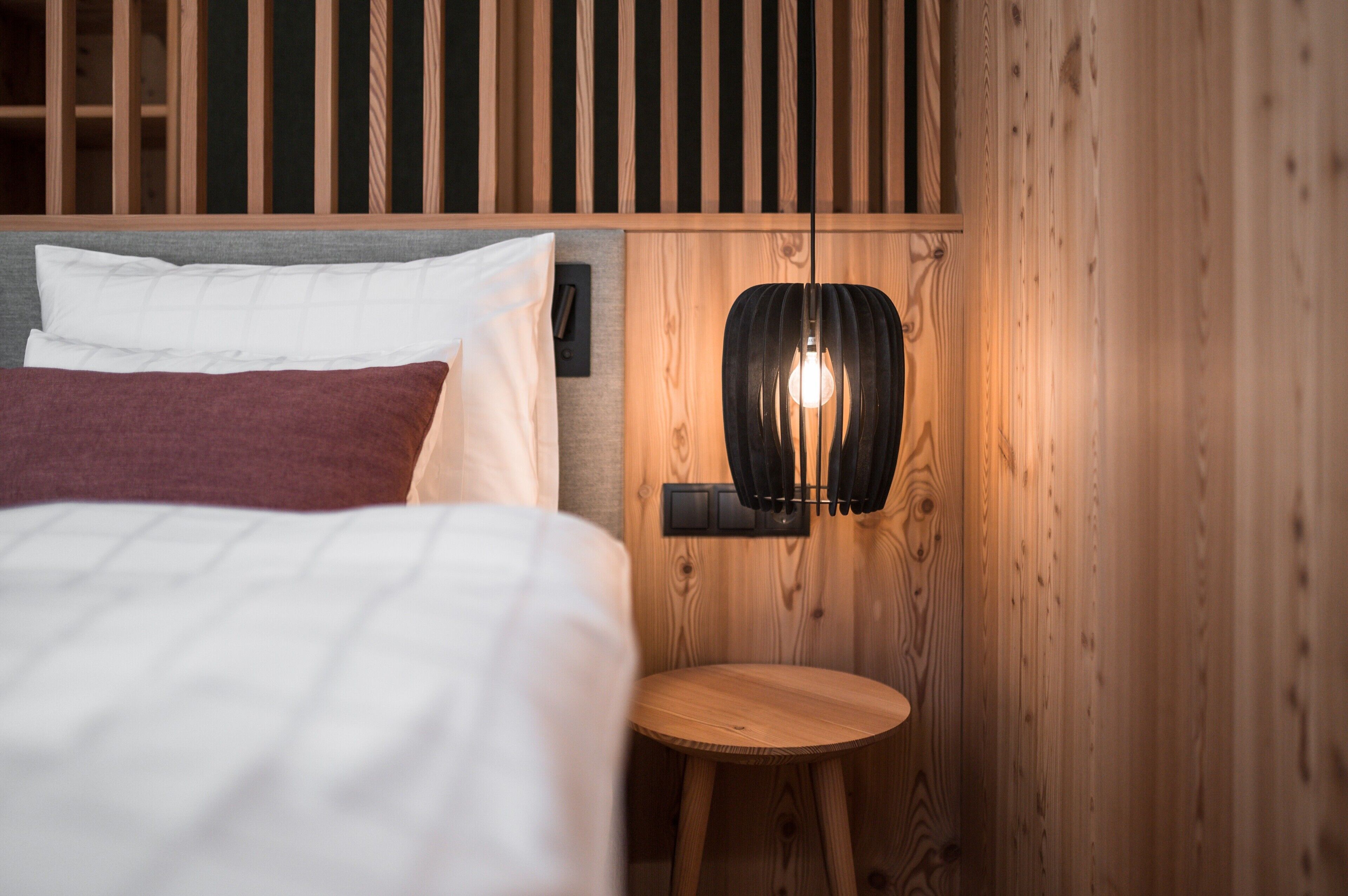 Une pièce en bois avec un lit, une petite table ronde et un luminaire fixé au mur.