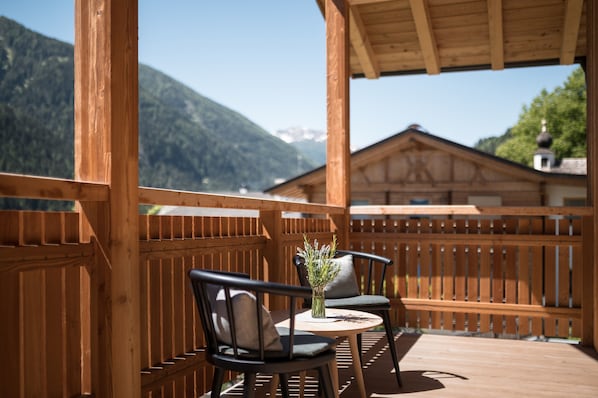 Eine Holzterrasse mit zwei Stühlen und einem Tisch, mit Blick auf einen Berg.