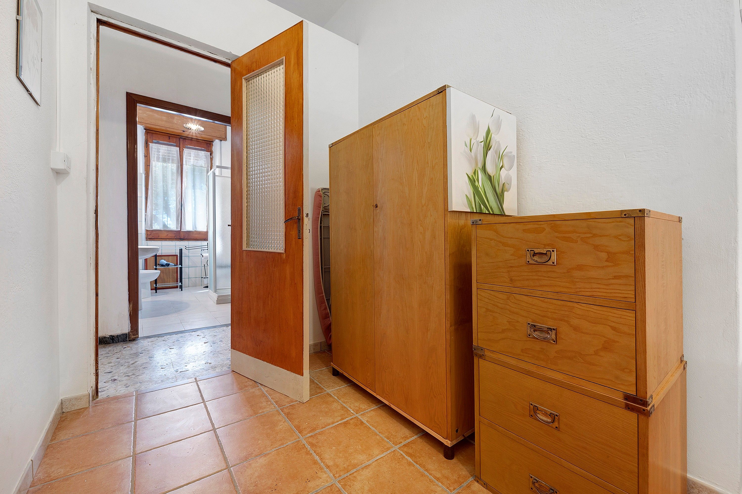 A hallway with a wooden wardrobe, a tiled floor, and a door leading to a bathroom.