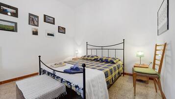 Ein Schlafzimmer mit einem Bett, einem Sessel, einem Nachttisch und einer Wand mit gerahmten Bildern.
