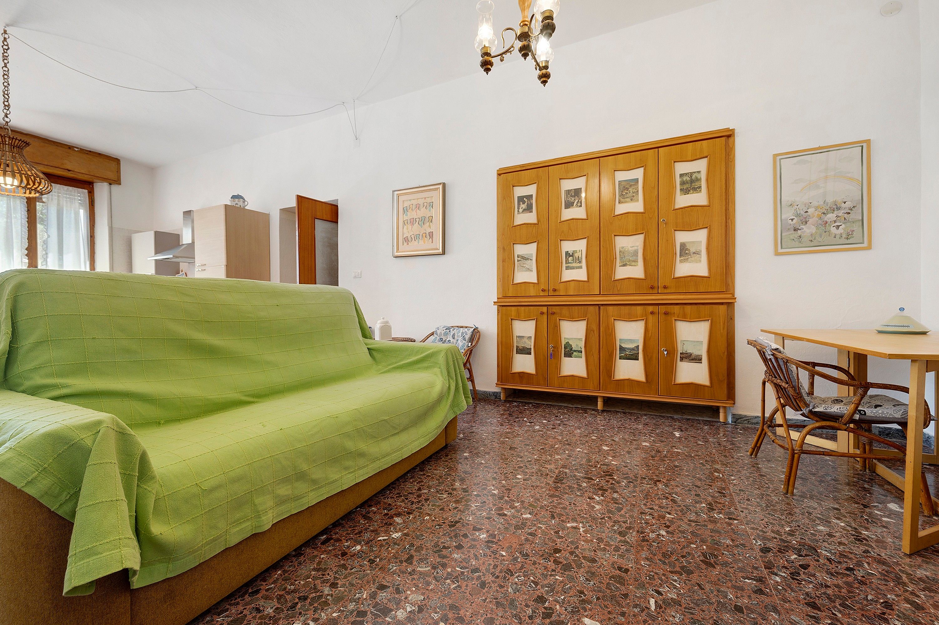 Una stanza con un divano verde, un armadio in legno con delle foto, un tavolo da pranzo con sedie e un lampadario.