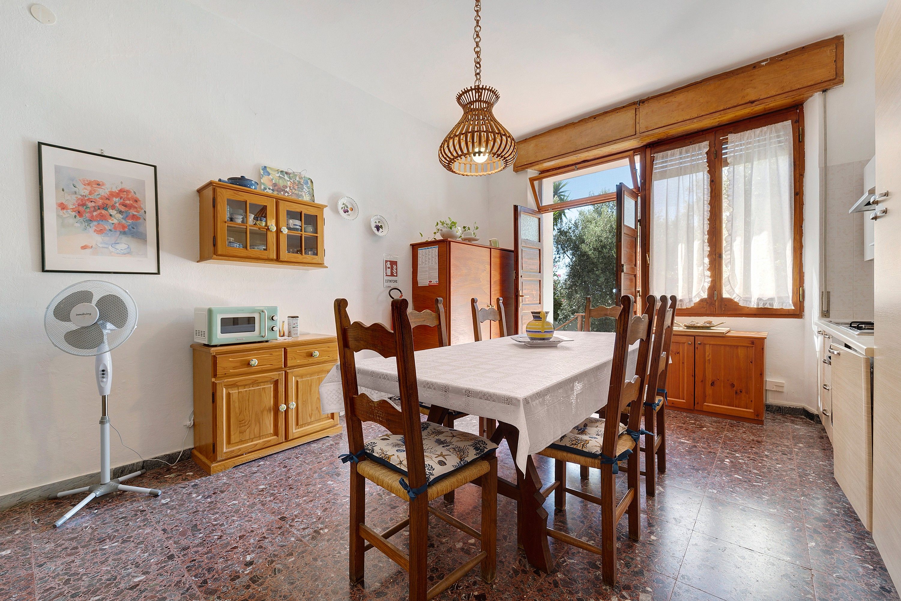 A dining area with a wooden table, chairs, a fan, and a cabinet.