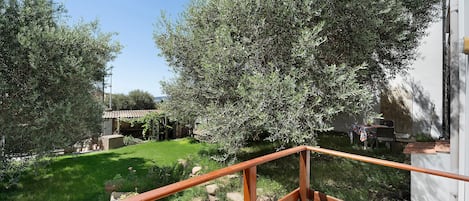 Un jardín con olivos, un muro de piedra y una barandilla de madera.