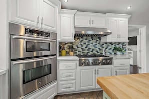 Uma cozinha com armários brancos, forno de aço inoxidável, fogão a gás e painel de azulejos.