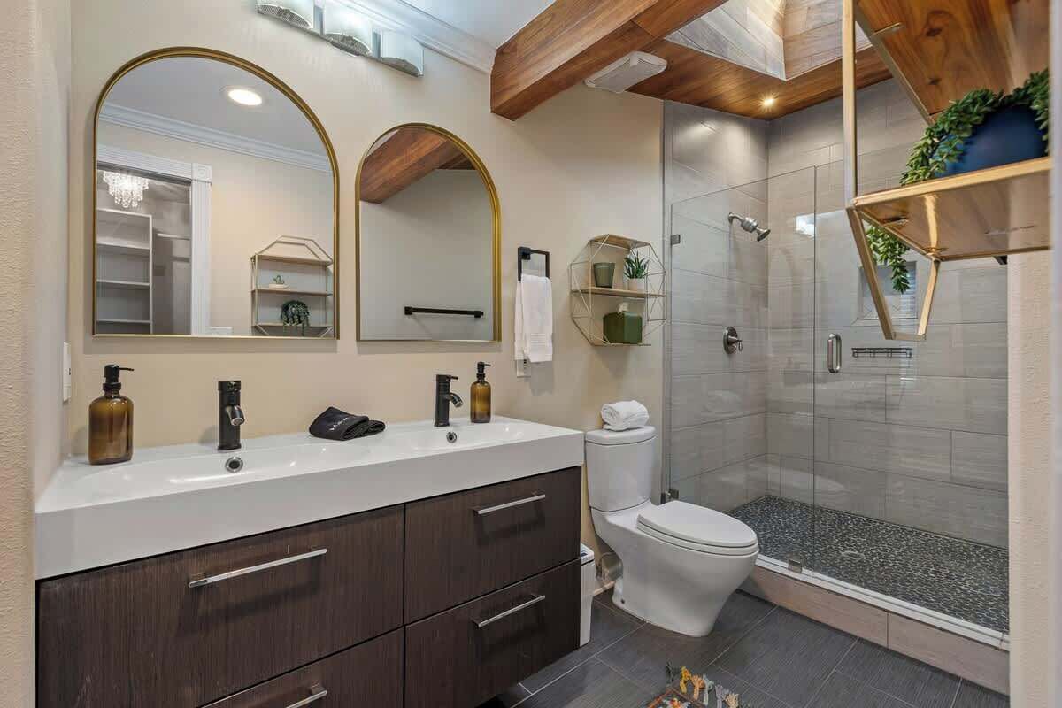Une salle de bain moderne comprenant un meuble-lavabo, deux miroirs, des toilettes et une douche à parois de verre.