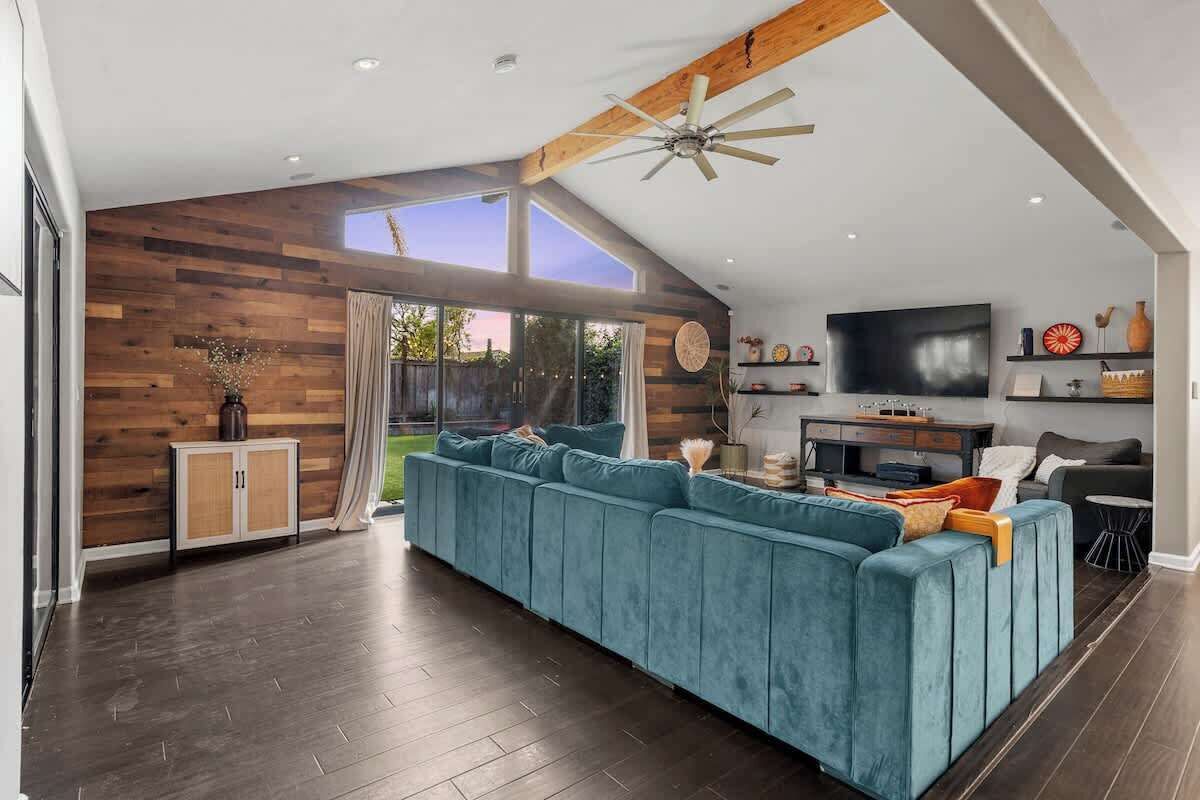 Una sala de estar moderna con un amplio sofá seccional azul, paneles de madera, un ventilador de techo y un televisor de pantalla plana.