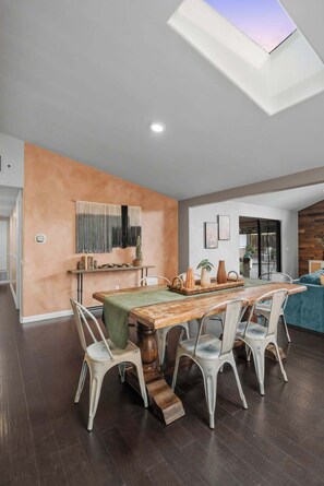 A dining area with a wooden table, white chairs, and a ceiling skylight. - The Murray, Modern Retreat, Spa & Billiards (San Diego)