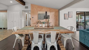 Un comedor con una gran mesa de madera, sillas blancas y un adorno central.