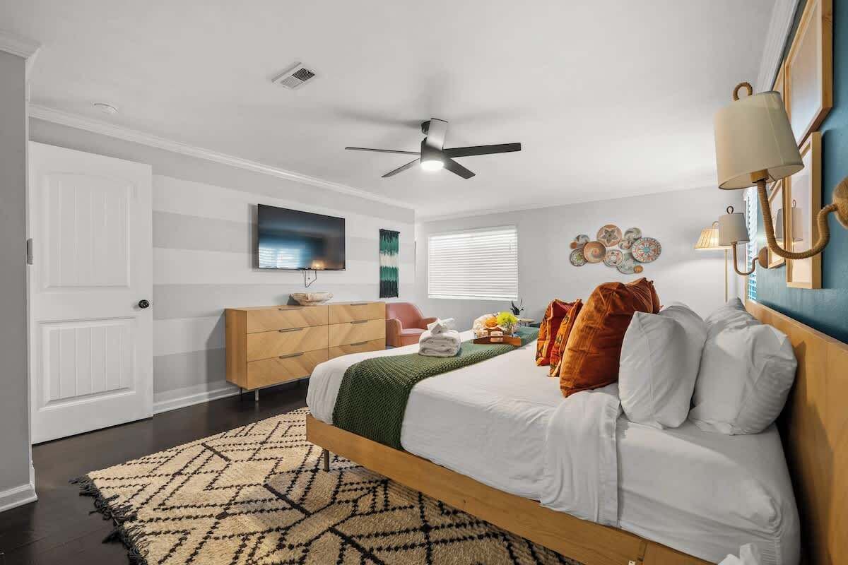 A bedroom with a bed, a ceiling fan, a dresser, a television, and a window with blinds.