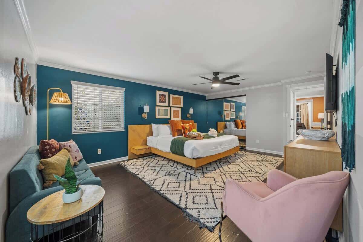 A bedroom with a bed, a sofa, a chair, a floor lamp, and a television.