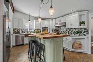 A modern kitchen with white cabinetry, a central island, and hanging pendant lights. - The Murray, Modern Retreat, Spa & Billiards (San Diego)