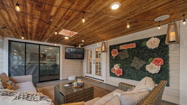 Una sala acogedora con techo de madera, un televisor de pantalla plana grande y un muro decorado con flores artificiales.