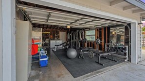 Un garaje con zona techada que contiene equipo de gimnasio, una pelota de ejercicio grande y un banco para pesas.