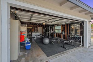 A garage with a covered area containing gym equipment, a large exercise ball, and a weight bench. - The Murray, Modern Retreat, Spa & Billiards (San Diego)