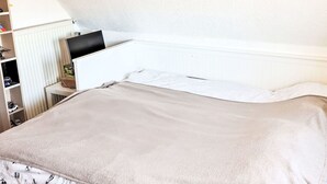 Une chambre à coucher avec un lit, un radiateur, un téléviseur posé sur un meuble et une étagère avec divers objets.