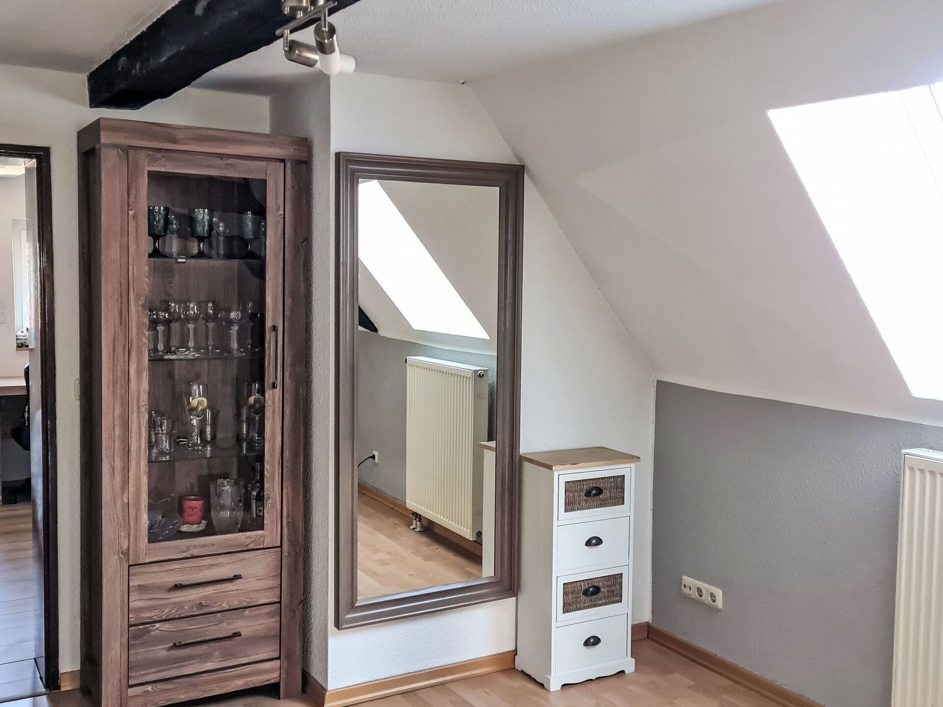 Ein Zimmer mit einem Holzkasten, einem großen Spiegel, einem Heizkörper und einem kleinen weißen Schrank.