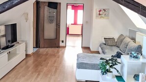 An attic room with a wooden floor, a white sofa, a TV, and a door leading to another room.