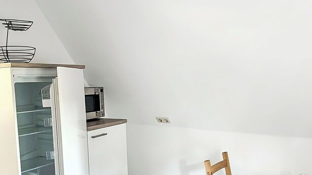 A dining area with a table set for two, a bowl of fruit, and a microwave above a white cabinet.