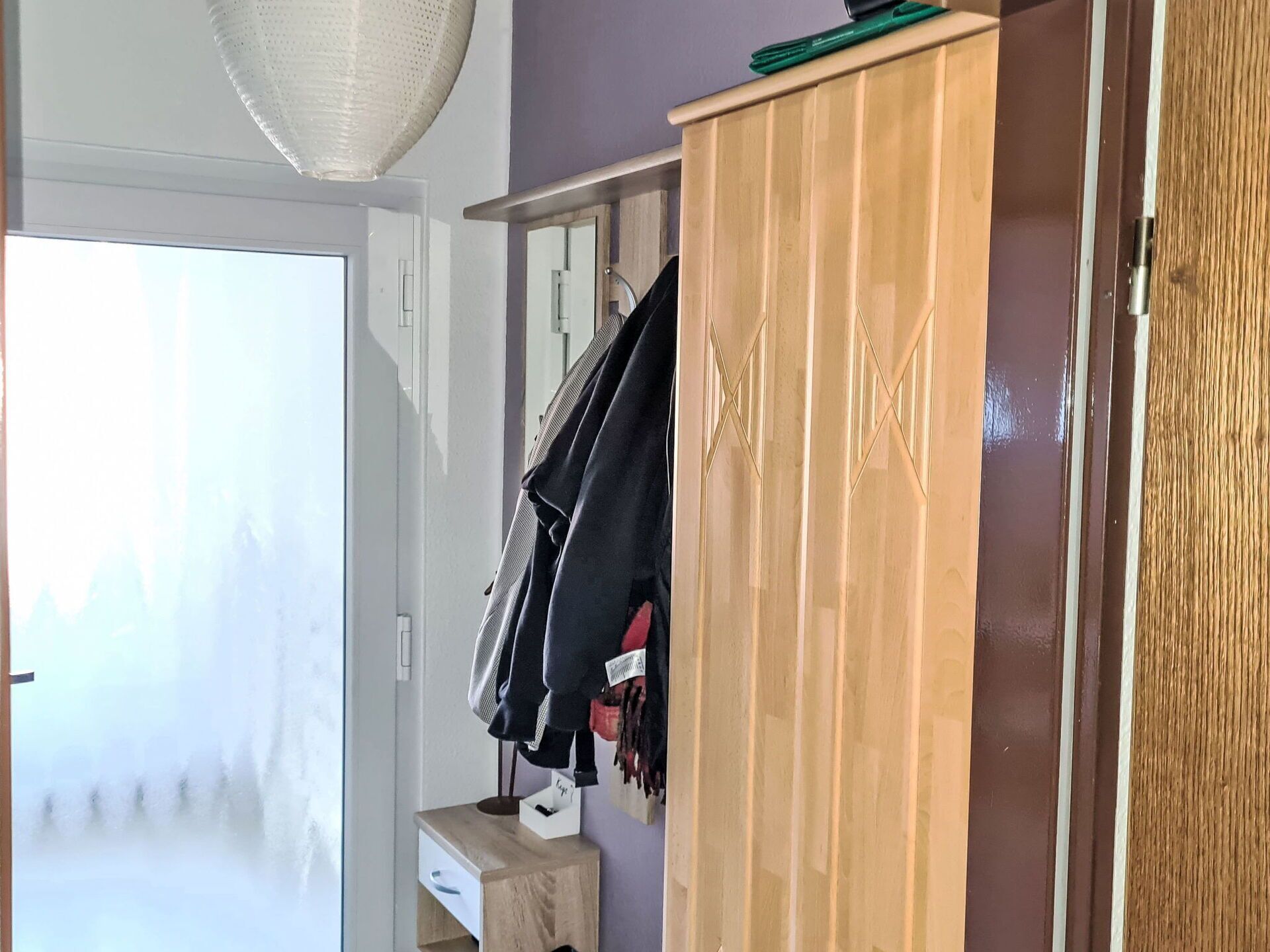 Ein Zimmer mit einem Holzschrank, einem kleinen Nachttisch mit Schublade und einem Kleiderhaken.