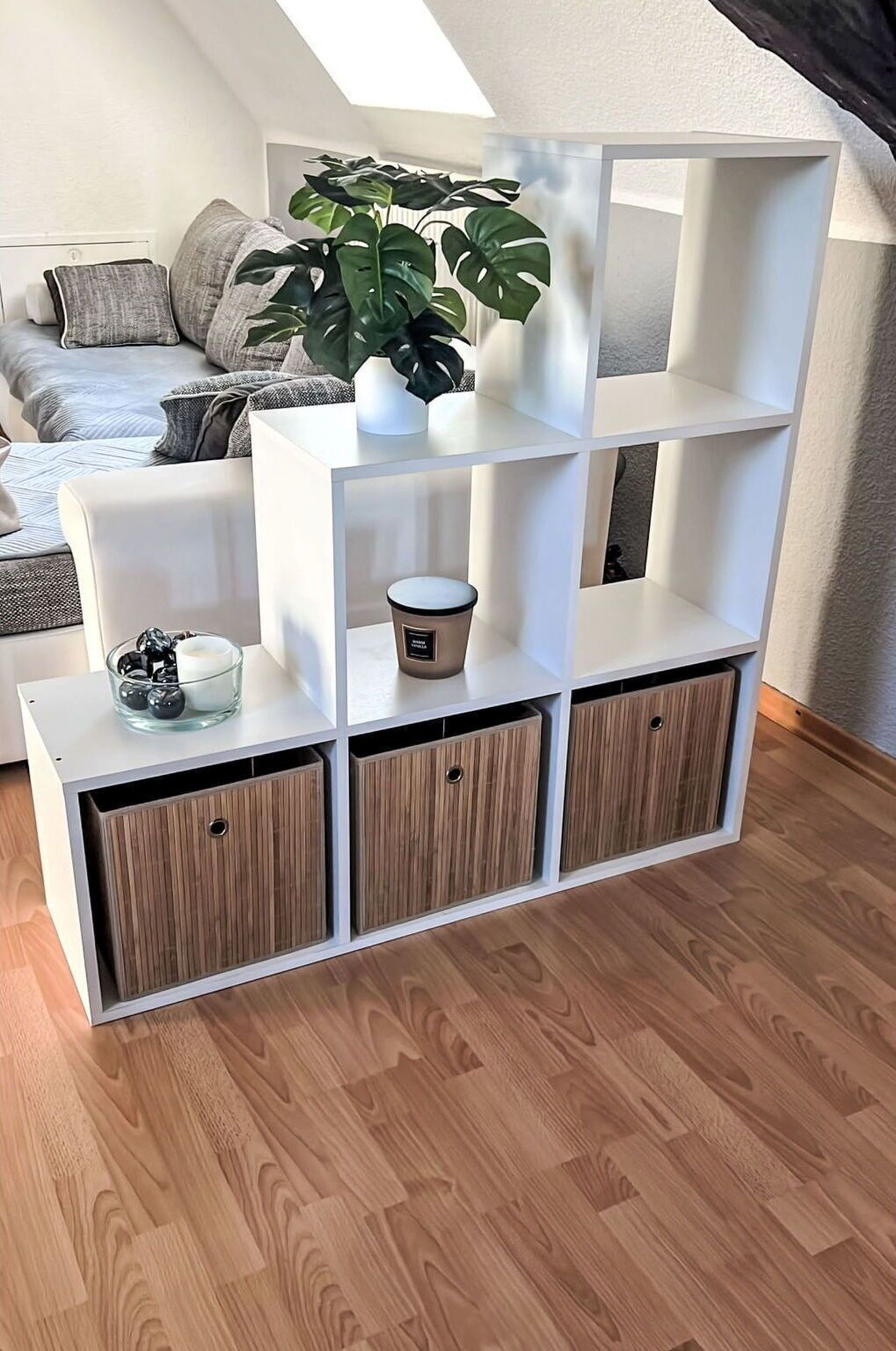 Ein weißes Regalsystem mit drei offenen Regalen und zwei geschlossenen Schränken, einer Topfpflanze und einer Kaffeetasse auf der obersten Ablage.