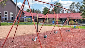 Ein Spielplatz mit Schaukeln und einem Gebäude im Hintergrund mit rotem Dach.