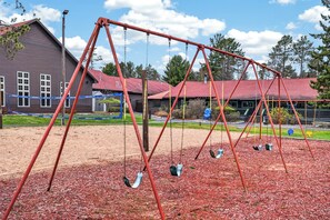Ein Spielplatz mit Schaukeln und einem Gebäude im Hintergrund mit rotem Dach.