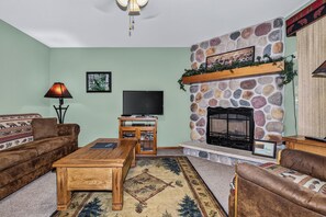Ein Wohnzimmer mit Kamin aus Stein, einem Fernseher und zwei Sofas.