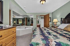 Ein Schlafzimmer mit einem großen Bett, einem separaten Badezimmer, einer Holzkommode und einem Telefon auf der Kommode.
