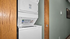 Eine weiße Waschmaschine und ein Trockner stehen übereinander in einer Diele mit einem hölzernen Türrahmen und einer hellgrünen Wand.
