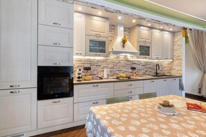 A kitchen with white cabinetry, a built-in oven, a stone backsplash, and a dining area with a table set for two.