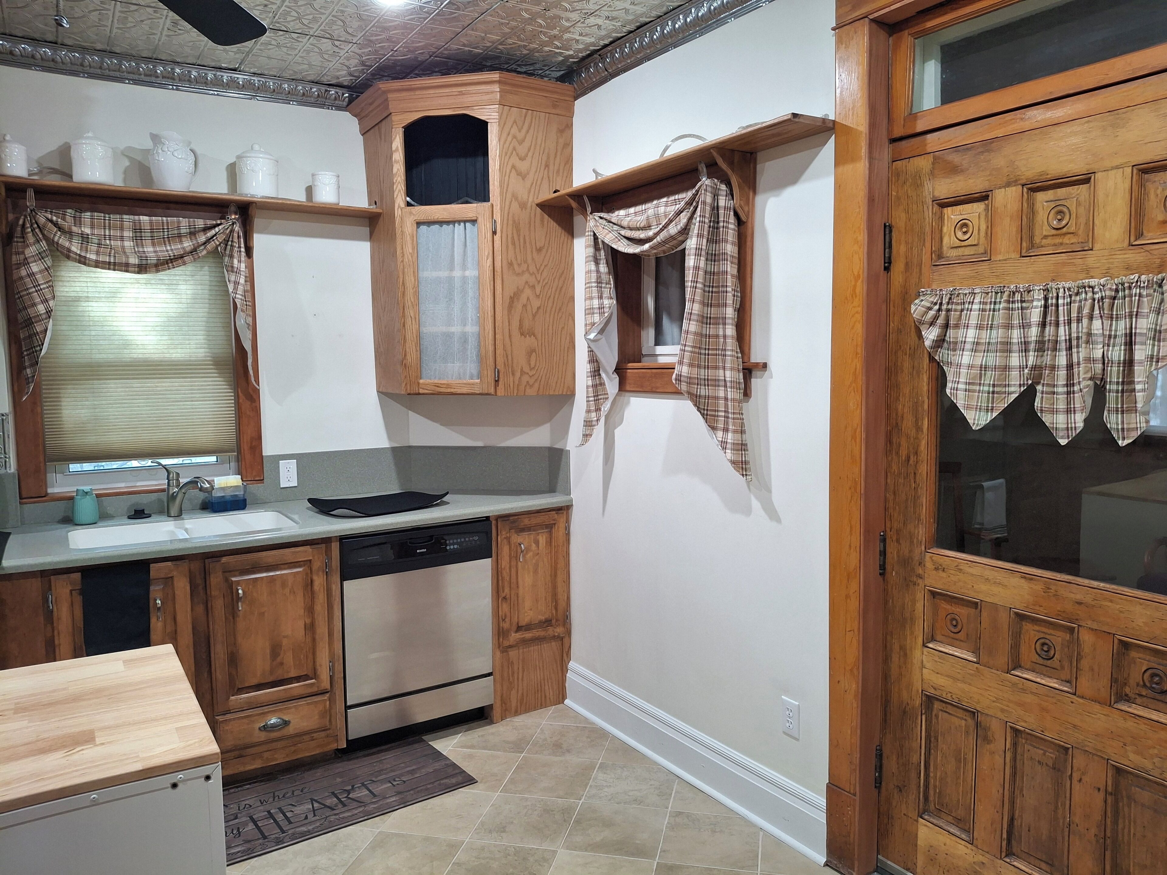 A kitchen with wooden cabinets, a built-in oven, a sink, and a window with plaid curtains.