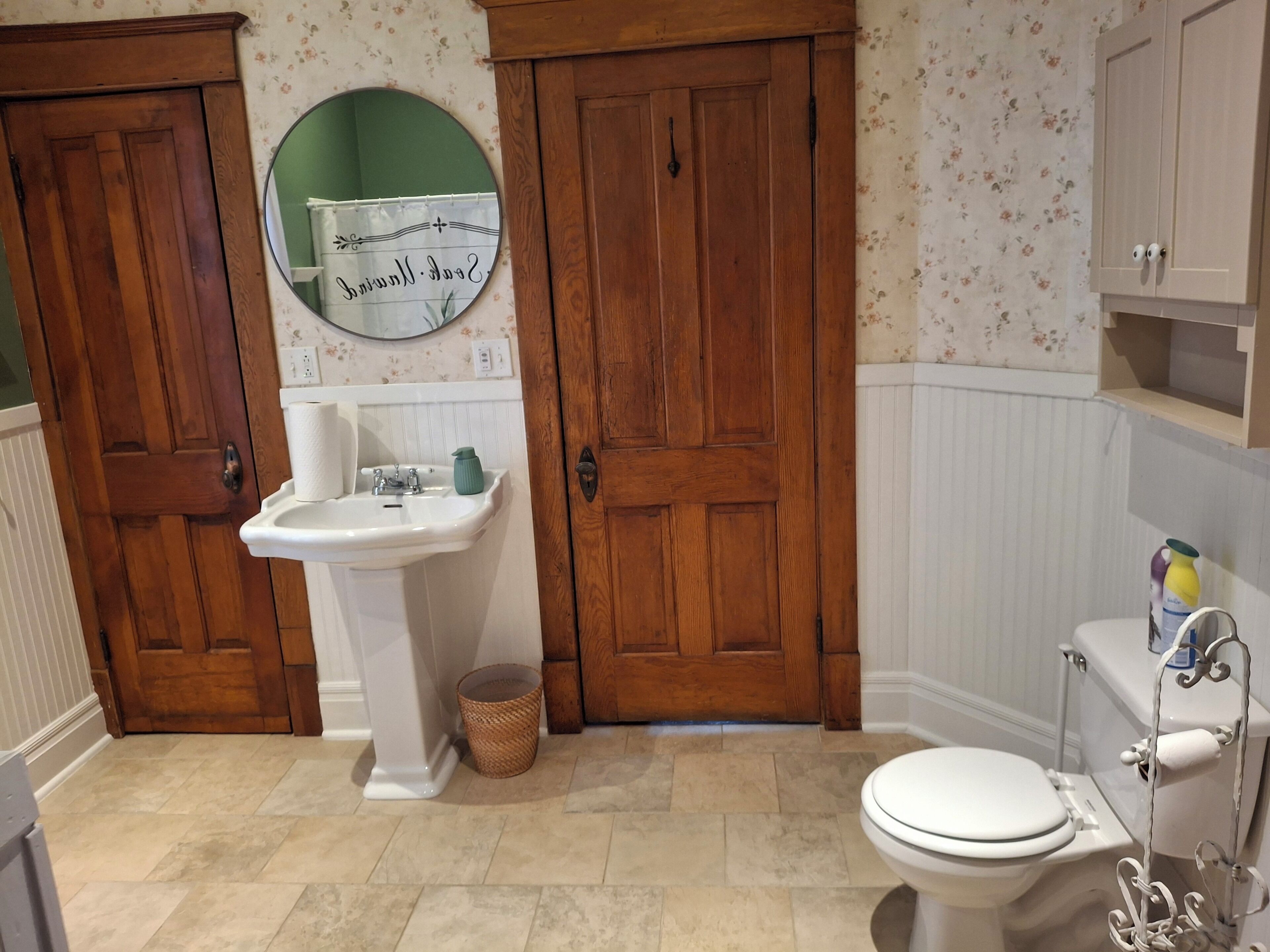A bathroom with a white sink, wooden doors, a toilet, and a mirror.