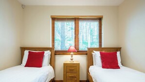A room with two beds, each with a wooden headboard, white bedding, and red pillows. There is a small wooden nightstand with a lamp between the beds. - Nice apartment for 4 guests with TV, patio and pets allowed (Coldstone)