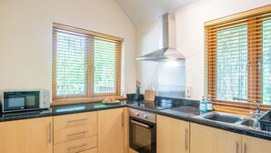 A kitchen with wooden cabinets, a microwave, an oven, a sink, and windows with blinds. - Nice apartment for 4 guests with TV, patio and pets allowed (Coldstone)