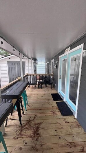 A covered porch with a wooden floor, a table, chairs, and a sliding glass door. - 1495 Ocean Lakes Golf Cart ⛱️🏝️🩱🌊👙☀️🐚 (Myrtle Beach)