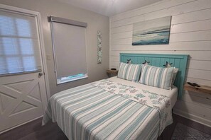 Ein Schlafzimmer mit einem Bett, einem Fenster mit Jalousien, einem Bild an der Wand und einem kleinen Nachttisch.